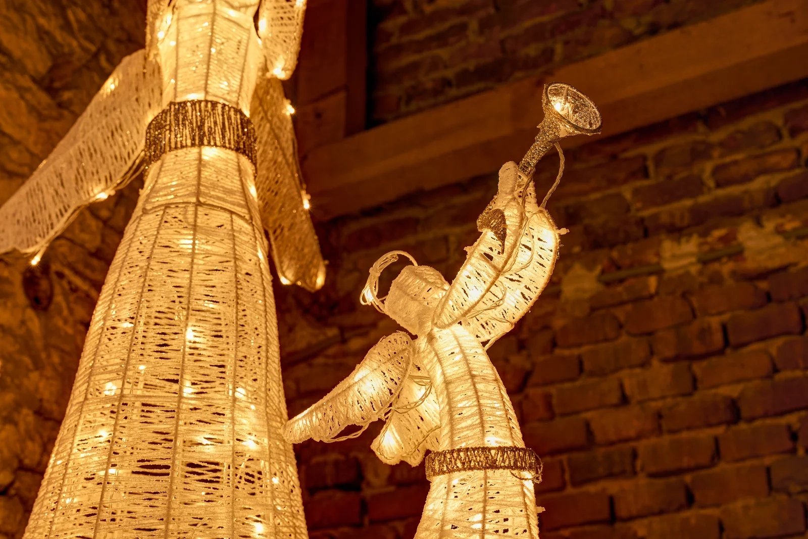 Světelný 3D LED anděl s trubkou 122 cm v teple bílé se dvěma malými anděly u kamenné zdi, DECOLED 3DA1W